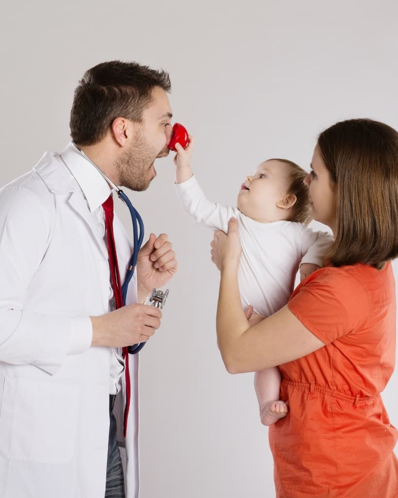 A paediatrician greeting a baby held by a parent before an appointment